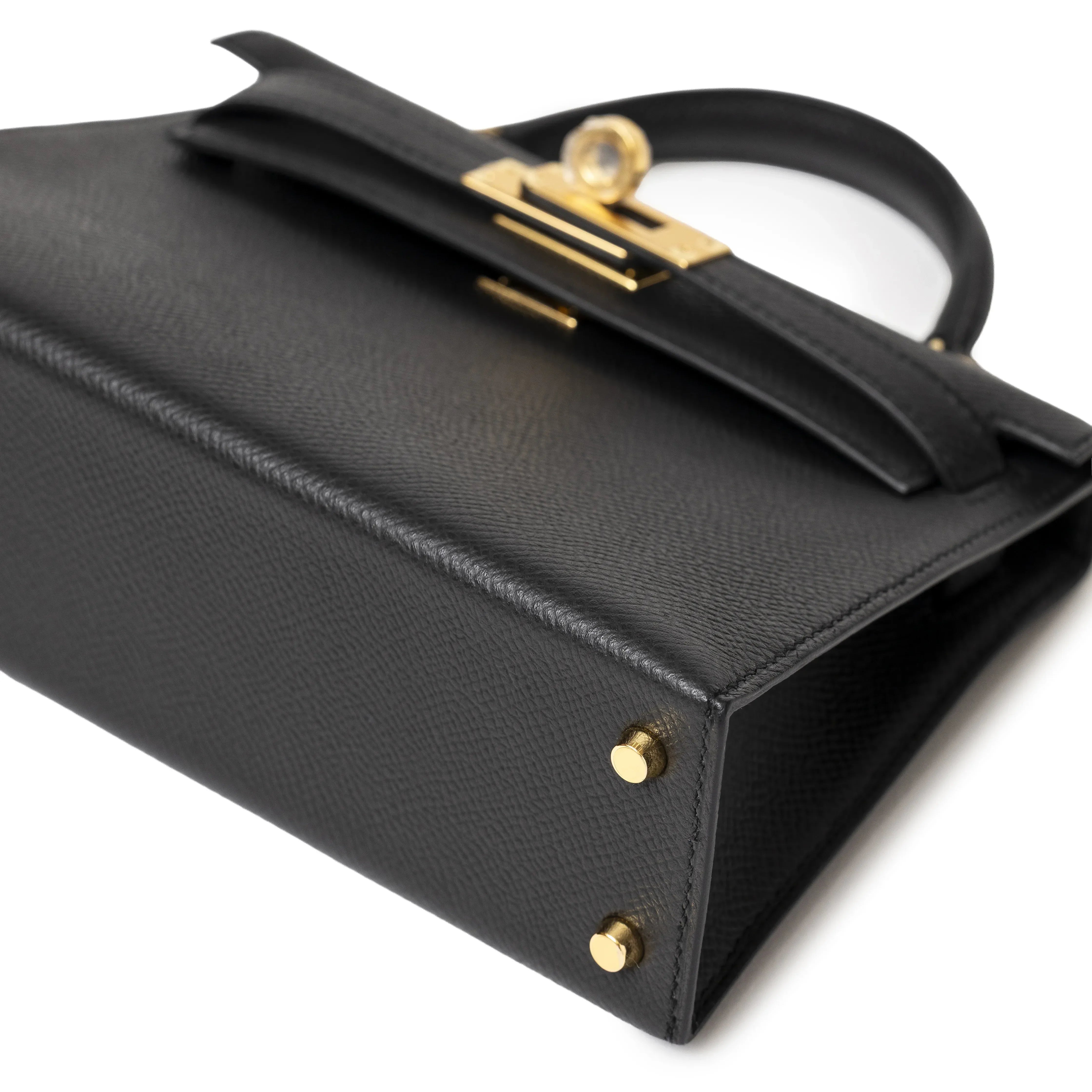 Black handbag with gold hardware, angled view showing handle and clasp details.