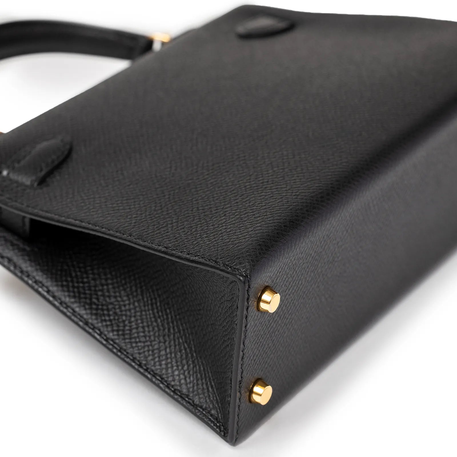 Black leather handbag bottom view with gold-tone studs and textured surface detail.