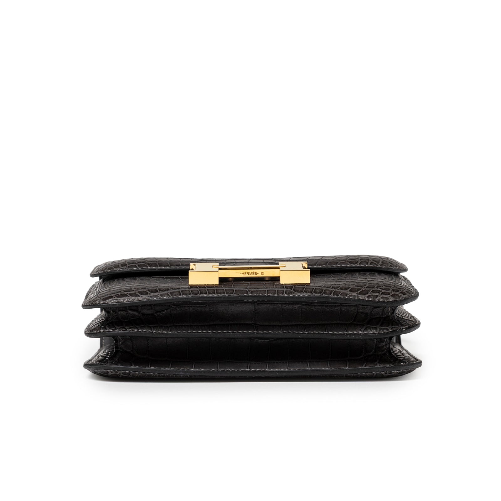 Bottom view of Hermès Mini Constance 18 Graphite Matte Alligator Gold Hardware showing layered alligator leather and gold clasp