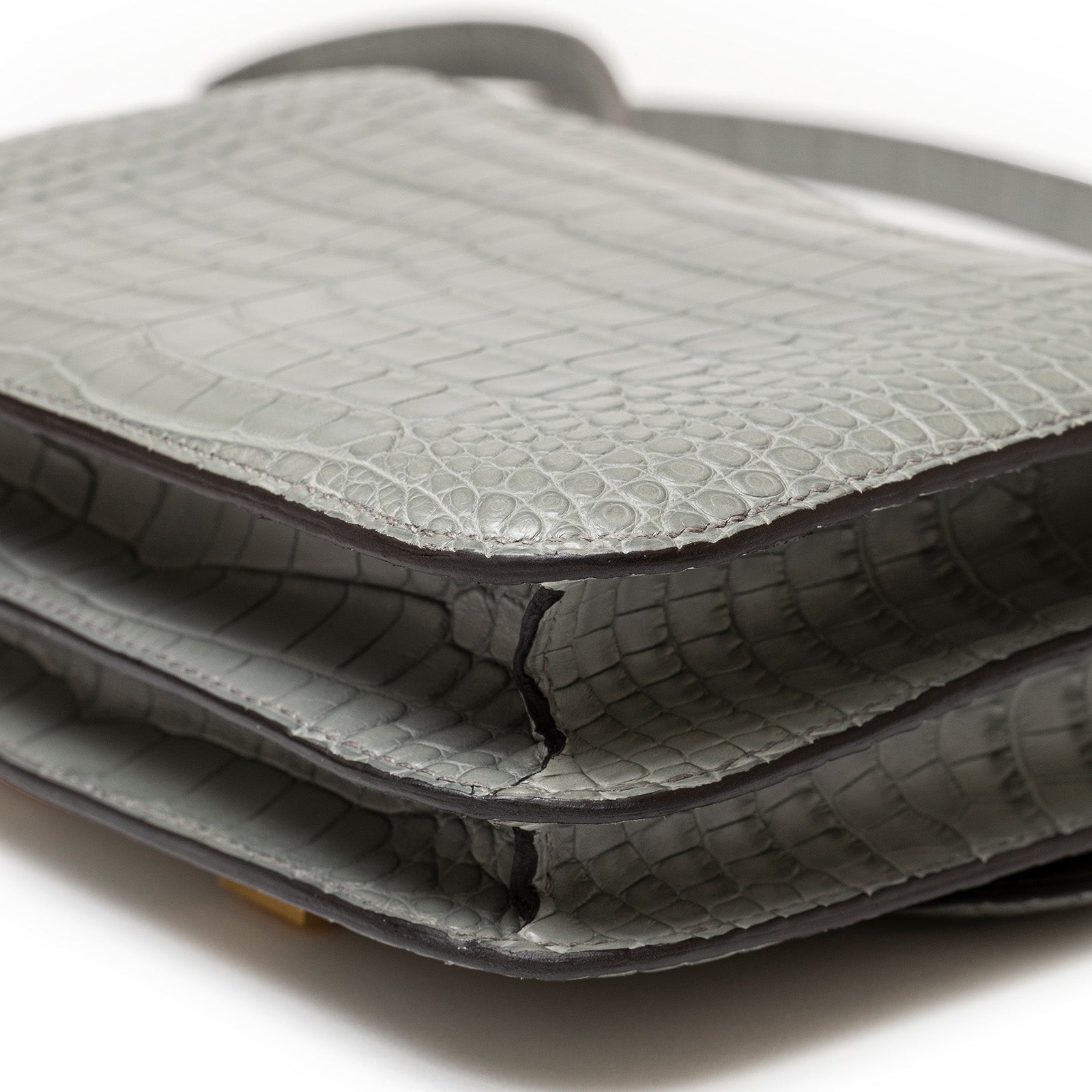 Close-up angled shot of Hermès Mini Constance 18 Gris Ciment Matte Alligator Gold Hardware texture and edge details