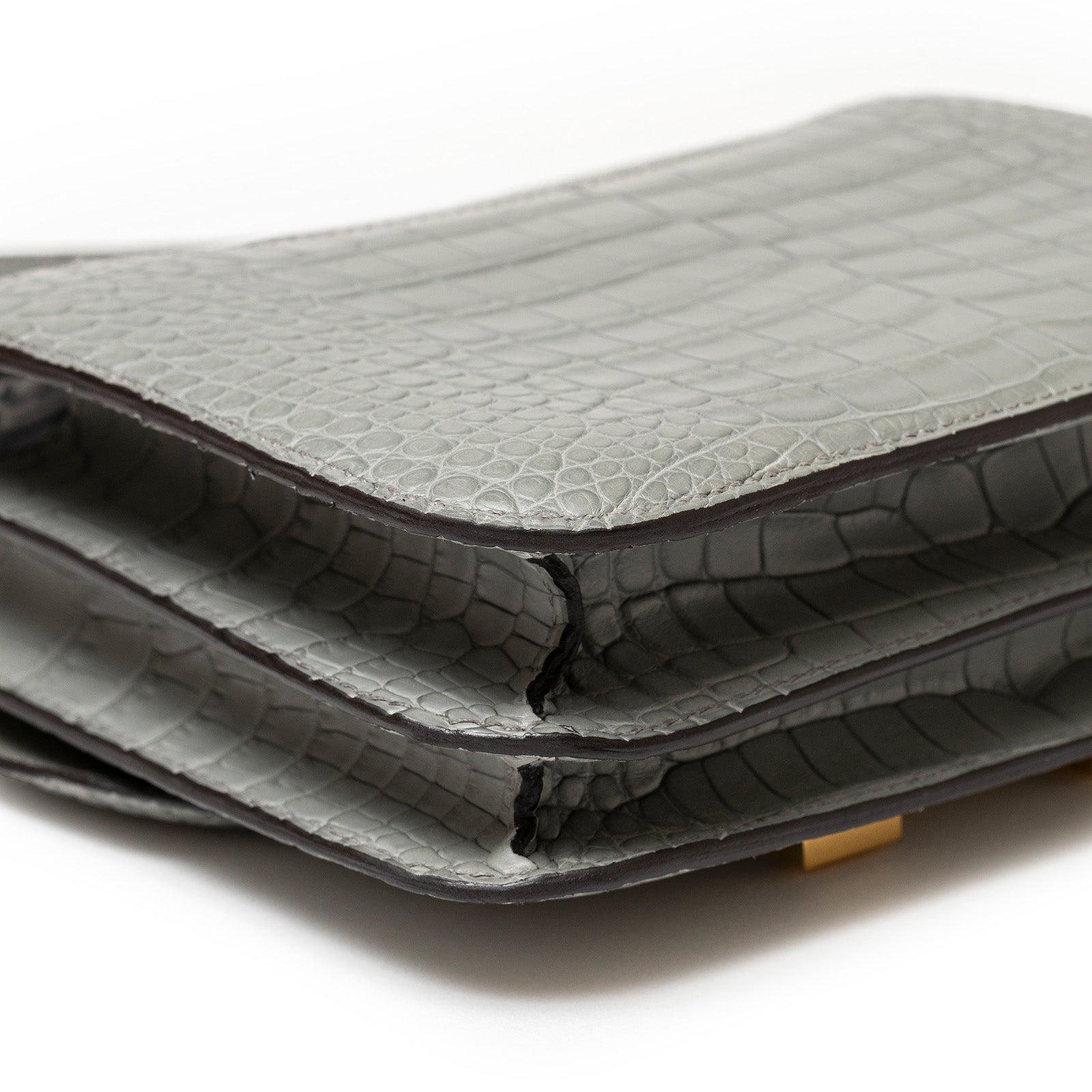 Close-up side view of Hermès Mini Constance 18 Gris Ciment Matte Alligator Gold Hardware highlighting texture and structure.