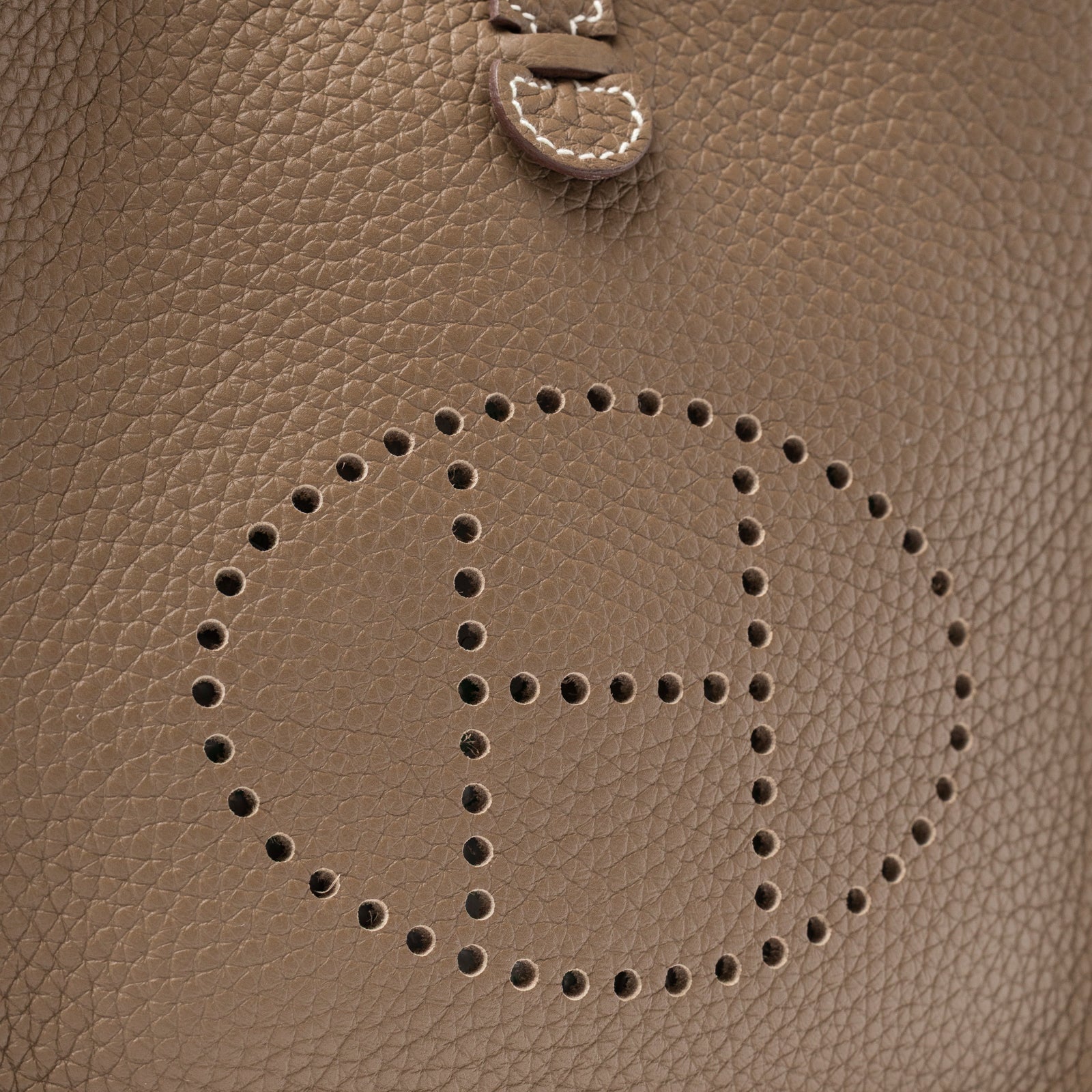 Close-up of Hermès Mini Evelyne Etoupe Blue Indigo Clemence Gold Hardware showing perforated H logo and grain texture detail