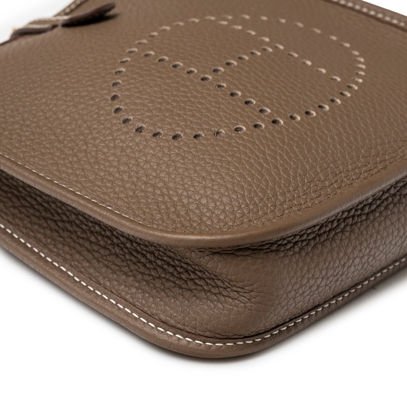 Close-up of corner and perforated logo on Hermès Mini Evelyne Etoupe Blue Indigo Clemence Gold Hardware showing textured leather and white stitching