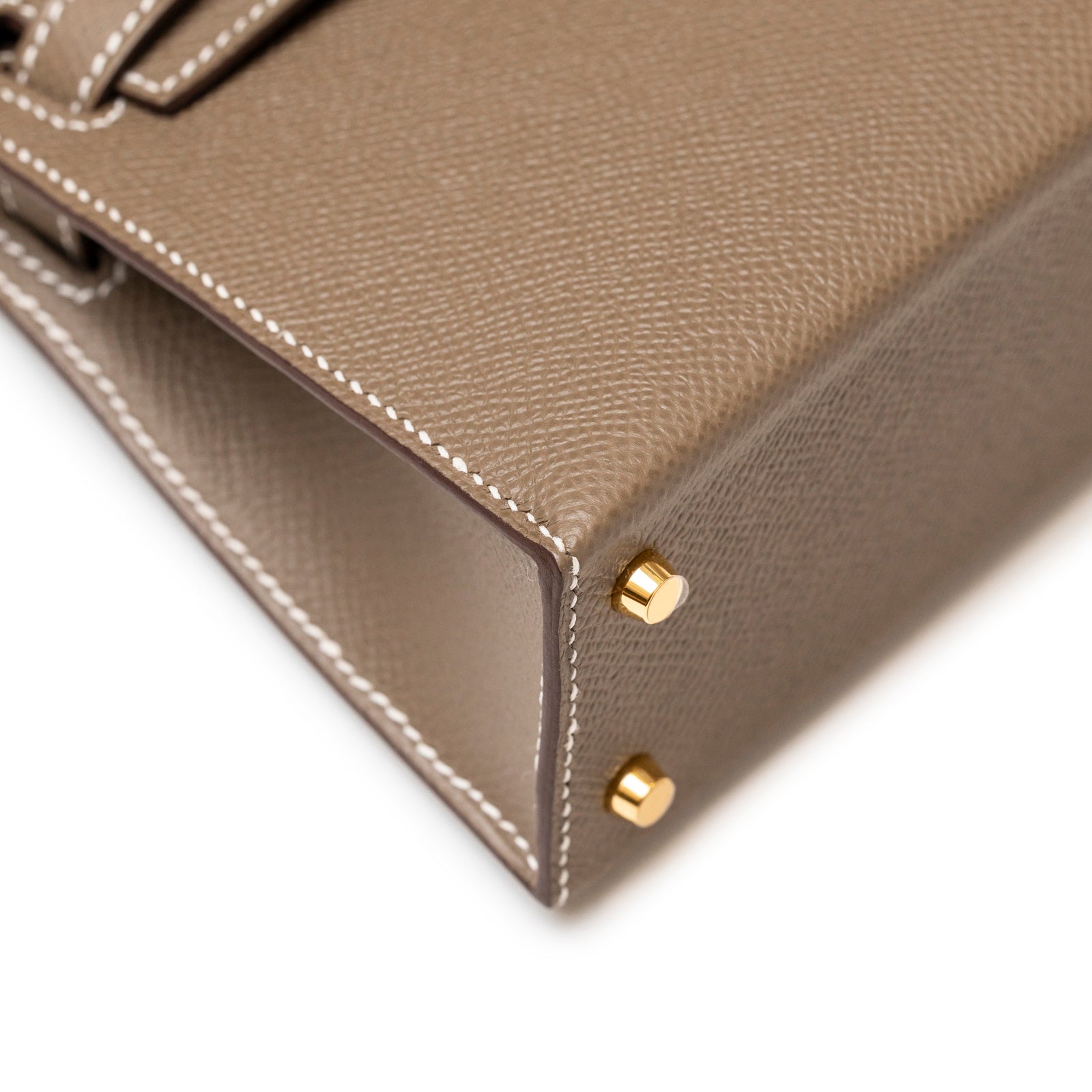 Close-up angled view of Hermès Mini Kelly II Sellier Etoupe Epsom Gold Hardware corner stitching and protective feet details