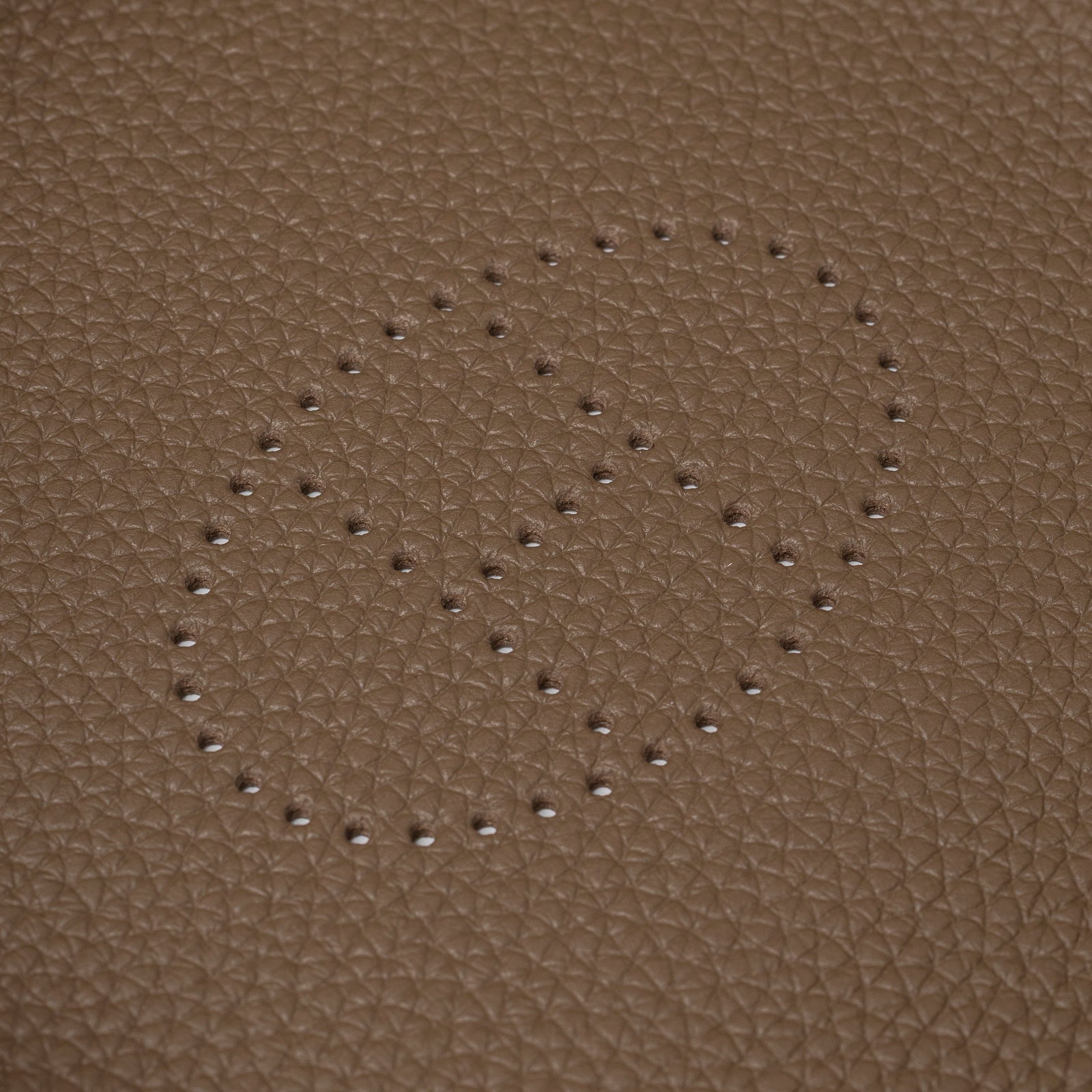 Close-up of perforated logo detail on pebbled leather surface of Hermès Mises et Relances H Evelyne Change Tray Etoupe Clemence
