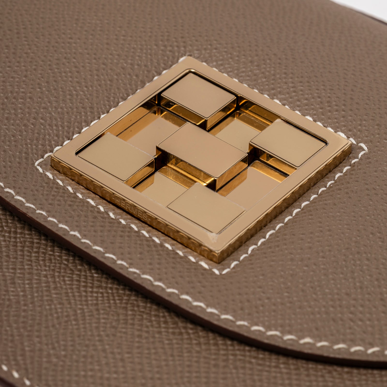 Close-up of Hermès Mosaique Au 24-17 Etoupe Epsom Permabrass Hardware showing gold clasp and contrasted white stitching detail