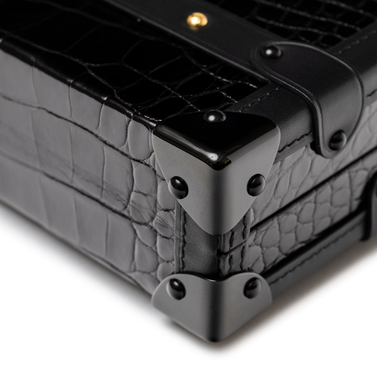 Close-up of Louis Vuitton Petite Malle Black Shiny Niloticus Gold Hardware corner showing polished croc embossing and black metal accents