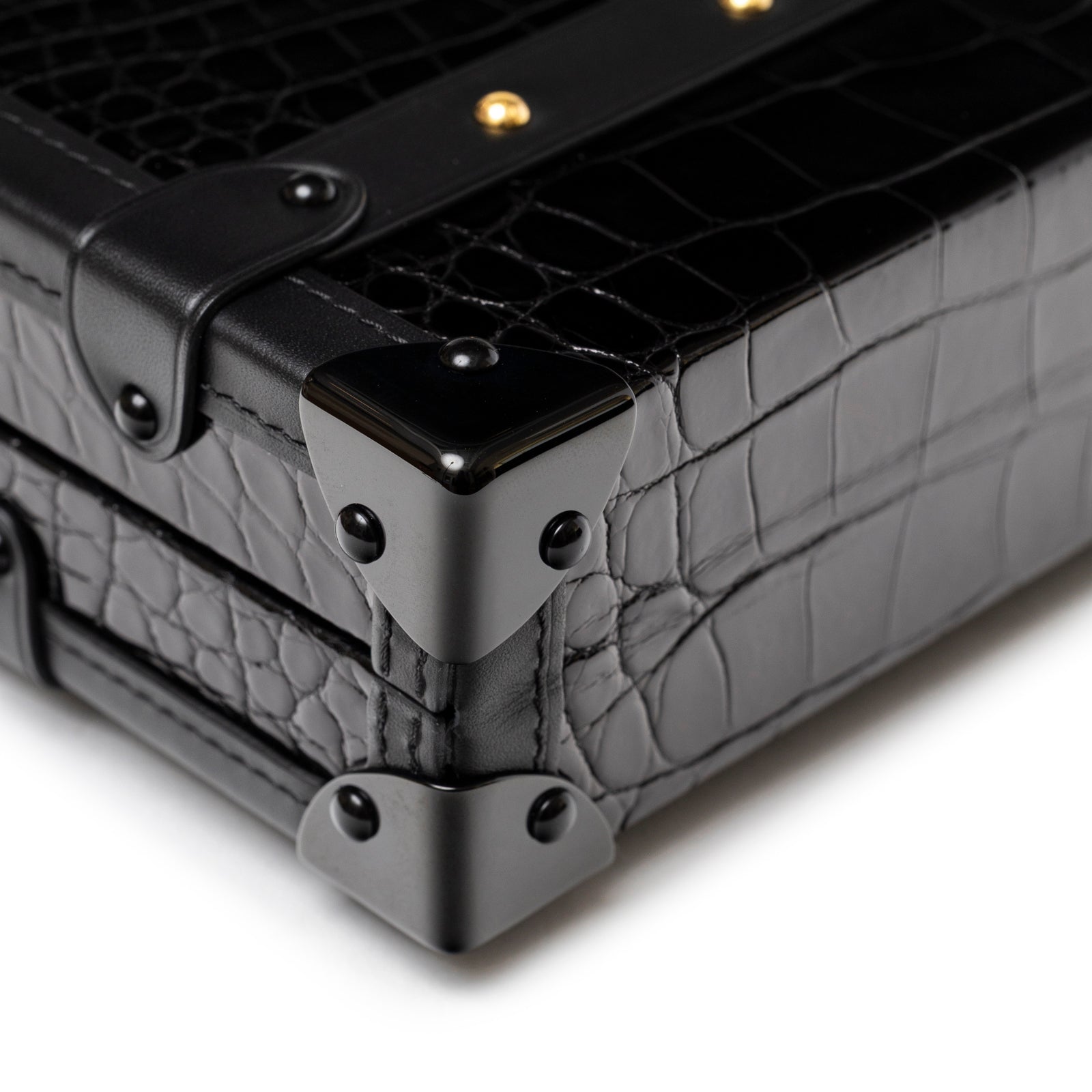 Close-up of Louis Vuitton Petite Malle Black Shiny Niloticus Gold Hardware corner with matte black corner protectors and croc texture