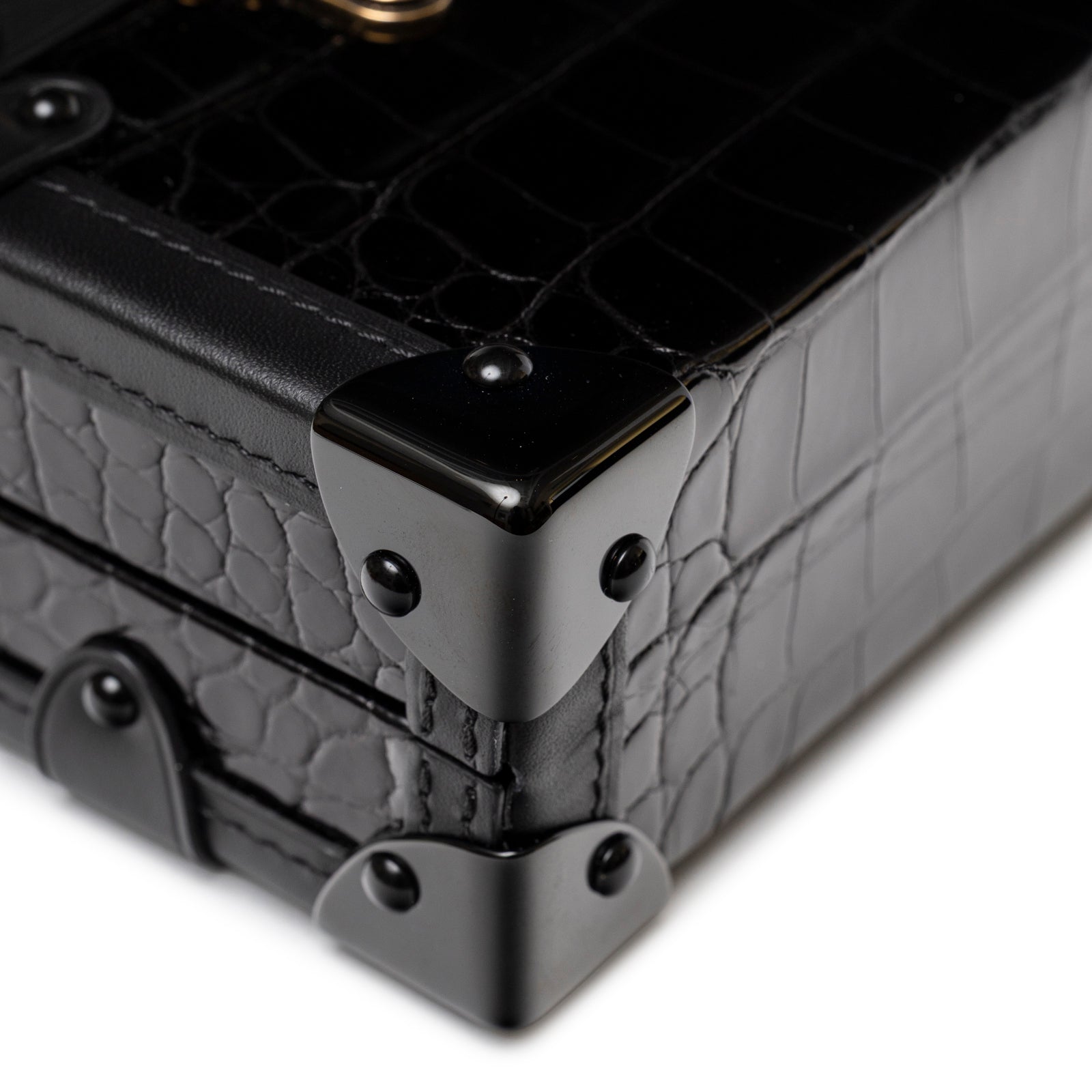Close-up of Louis Vuitton Petite Malle Black Shiny Niloticus Gold Hardware corner with glossy croc leather and metal studs detail