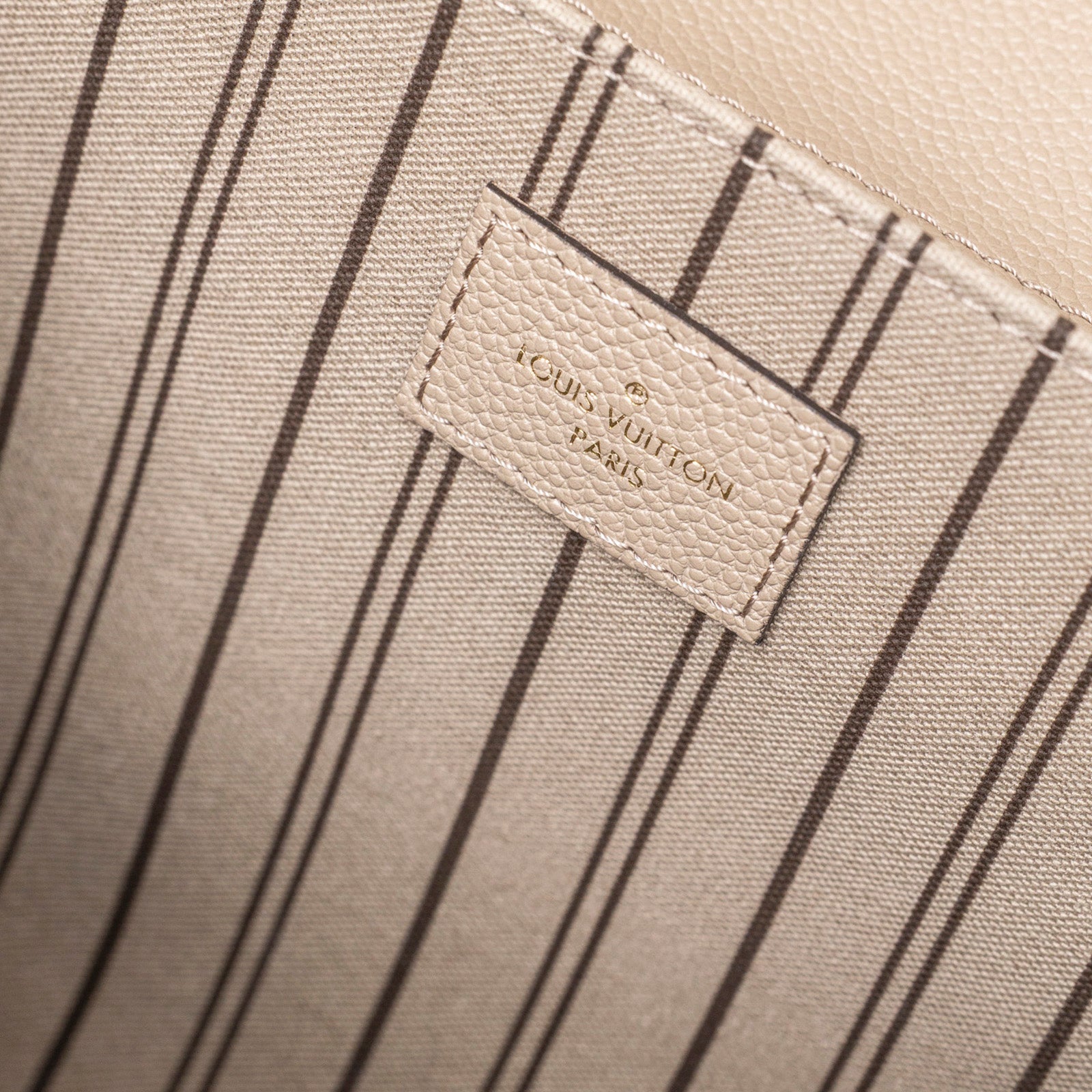 Close-up interior view of Louis Vuitton Pochette Métis Monogram Empreinte Turtledove Gold Hardware label and striped lining